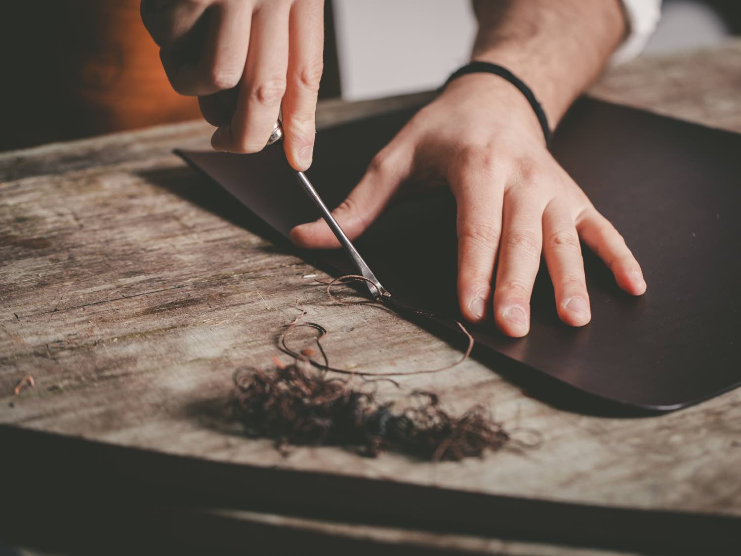 Le mani di Marta e Tommaso mentre tagliano il cuoio sul banco